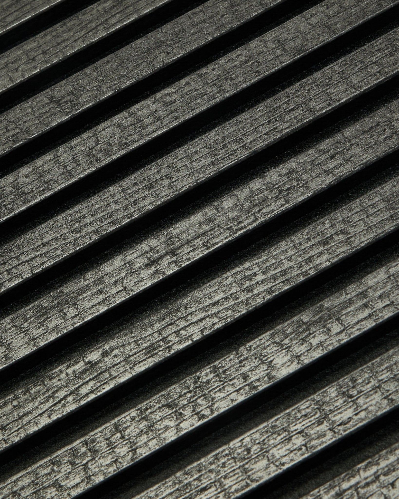 Close-up of WoodUpp Rebel Akupanel in Charcoal (240x60 cm) showing black, grooved acoustic slats arranged diagonally for enhanced sound absorption.