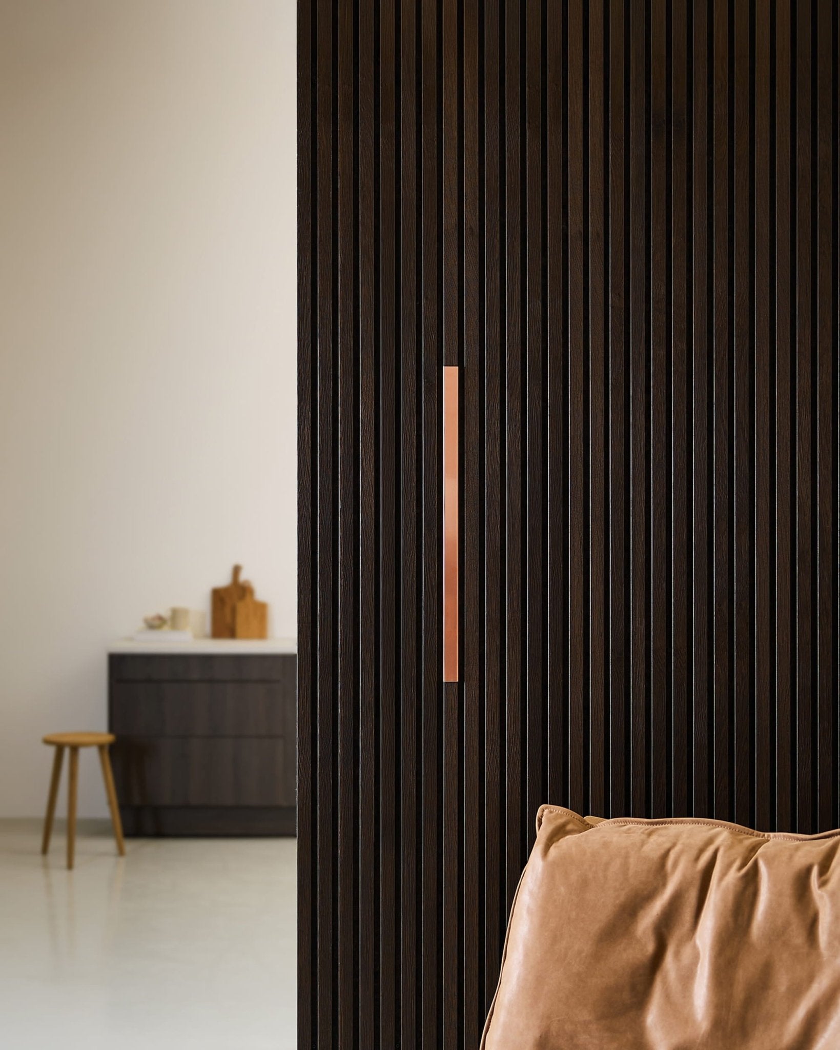 Minimalist kitchen with a WoodUpp Liva | Cover / Copper acoustic panel on a 60 cm wall, tan leather chair, stool, and countertop.