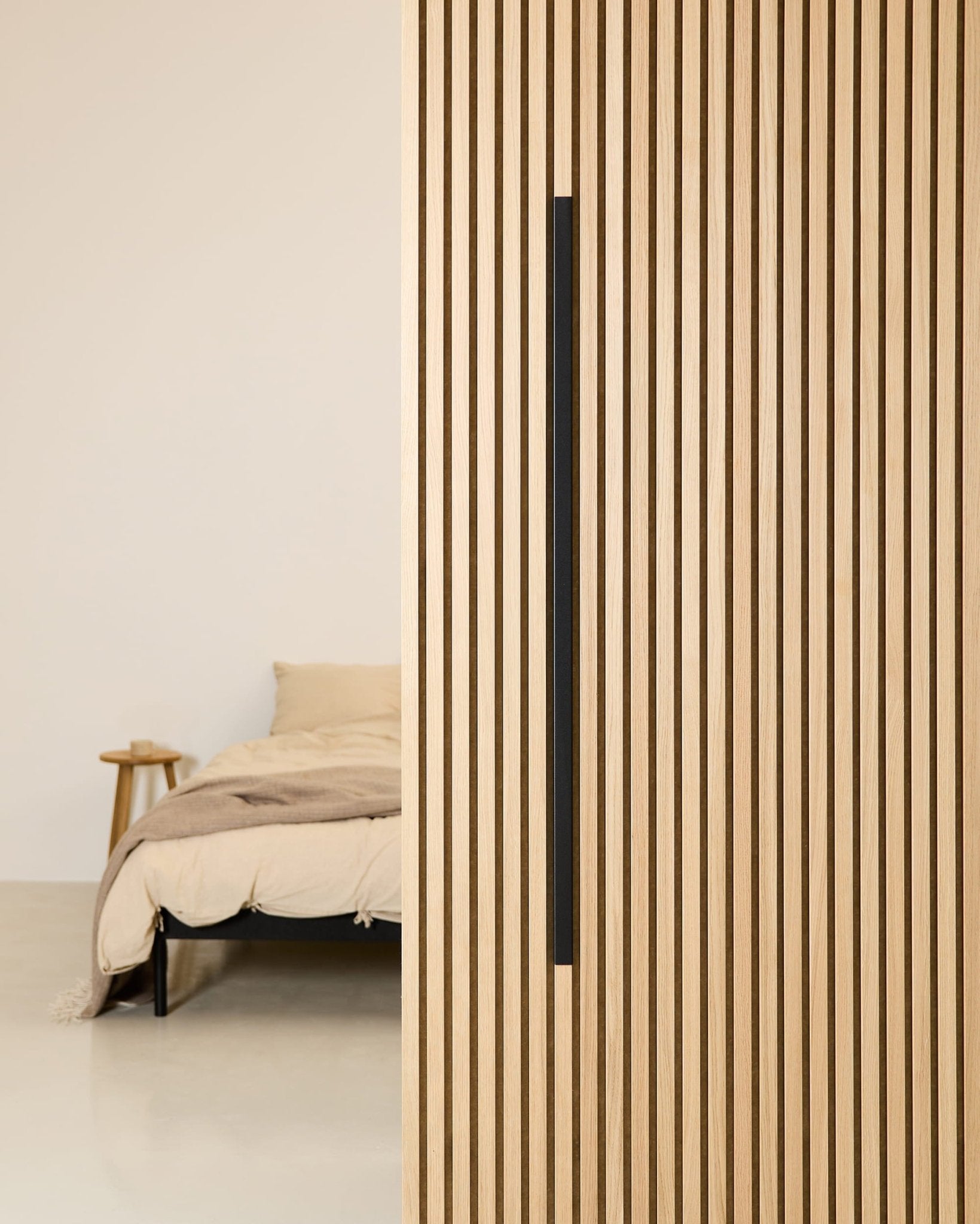 Minimalist bedroom with a beige bed, wooden side table, and a WoodUpp Akupanel Black Aluminum 120 cm acoustic panel mounted on the wall.