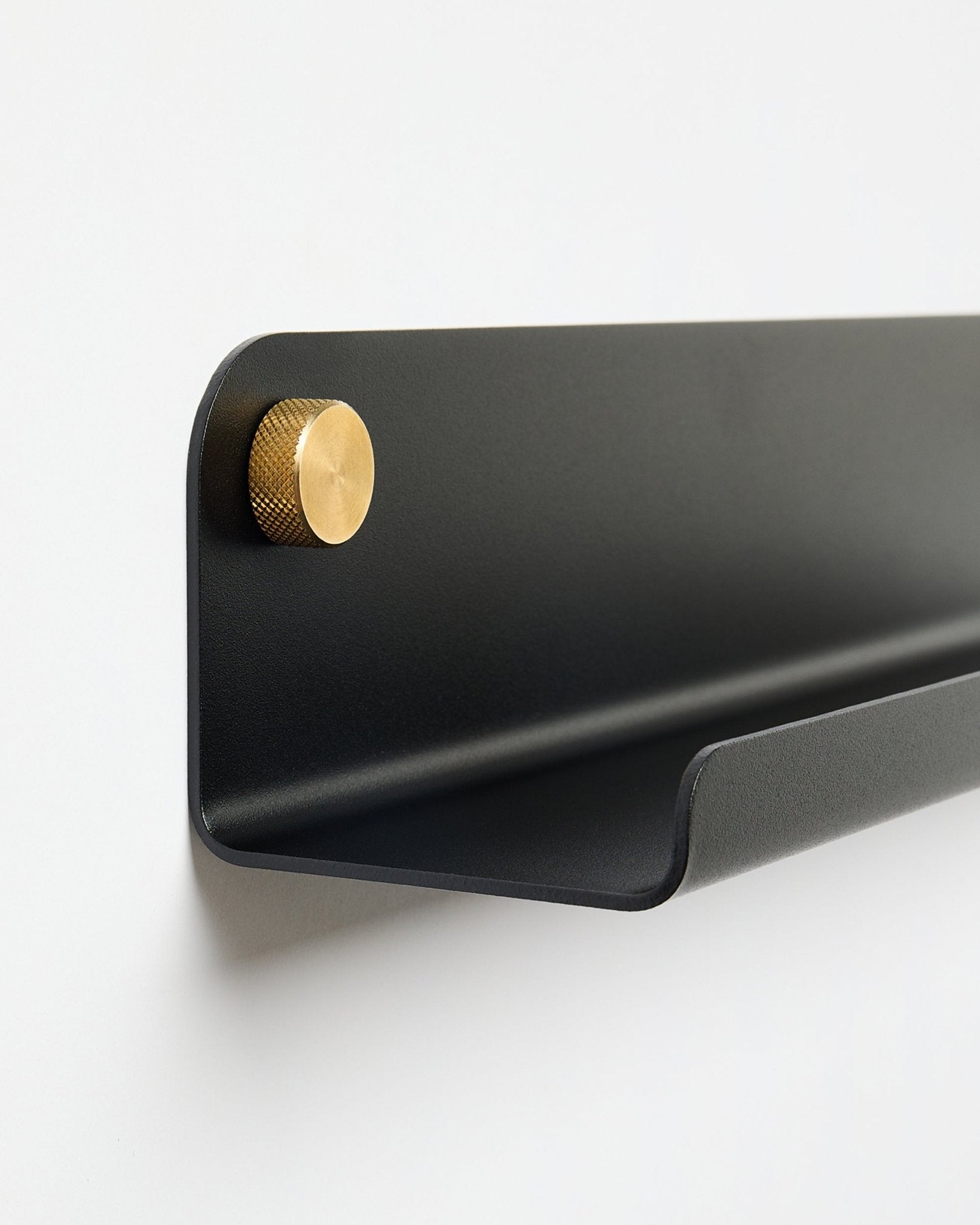 The Norr | Narrow Shelf in black (115.9 cm) with a single gold knob on the left, by WoodUpp, mounted on a plain white wall.