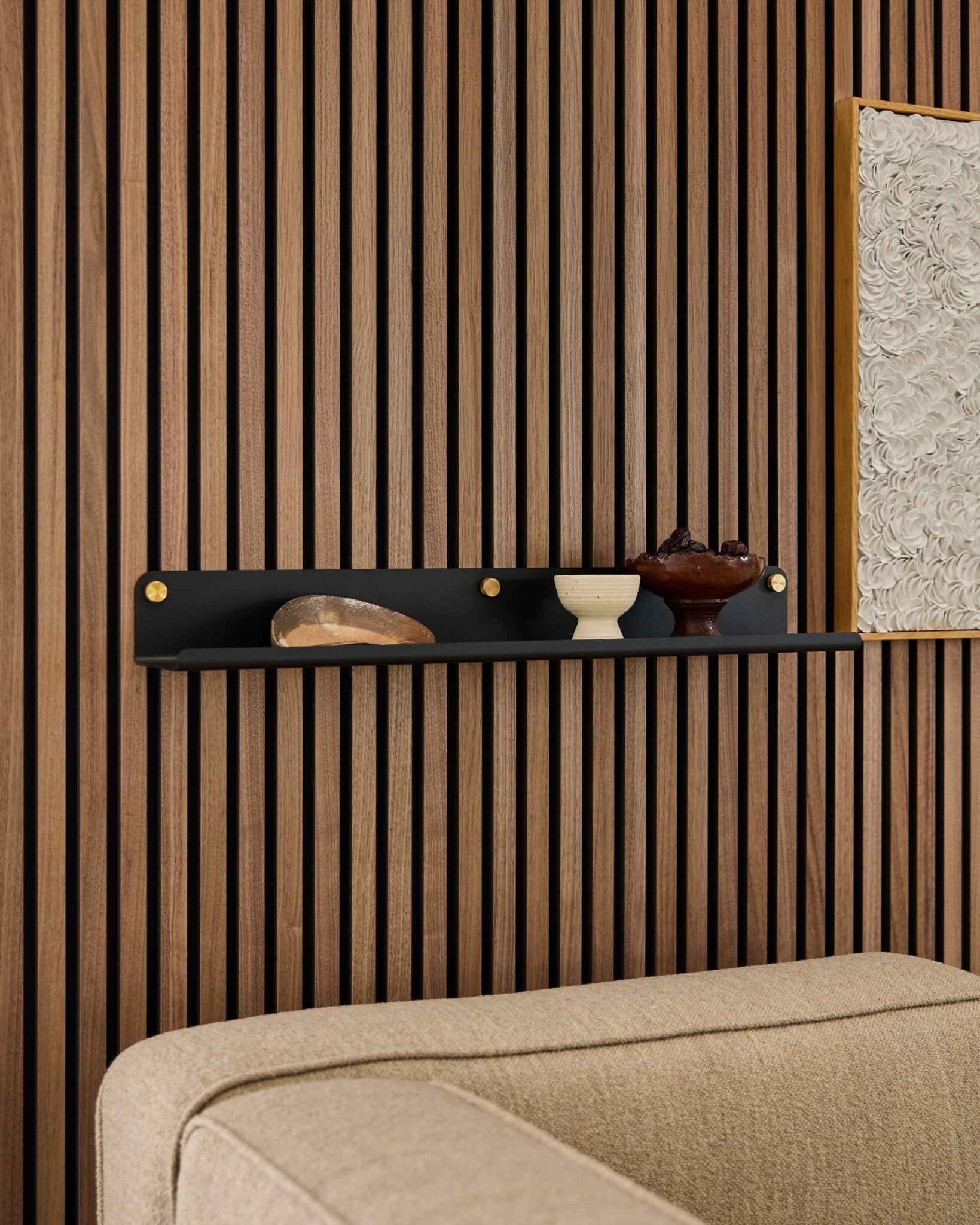 Black WoodUpp Norr Wide Shelf (75.9 cm) with decor above a beige sofa, mounted on a modern wooden acoustic slat wall panel.