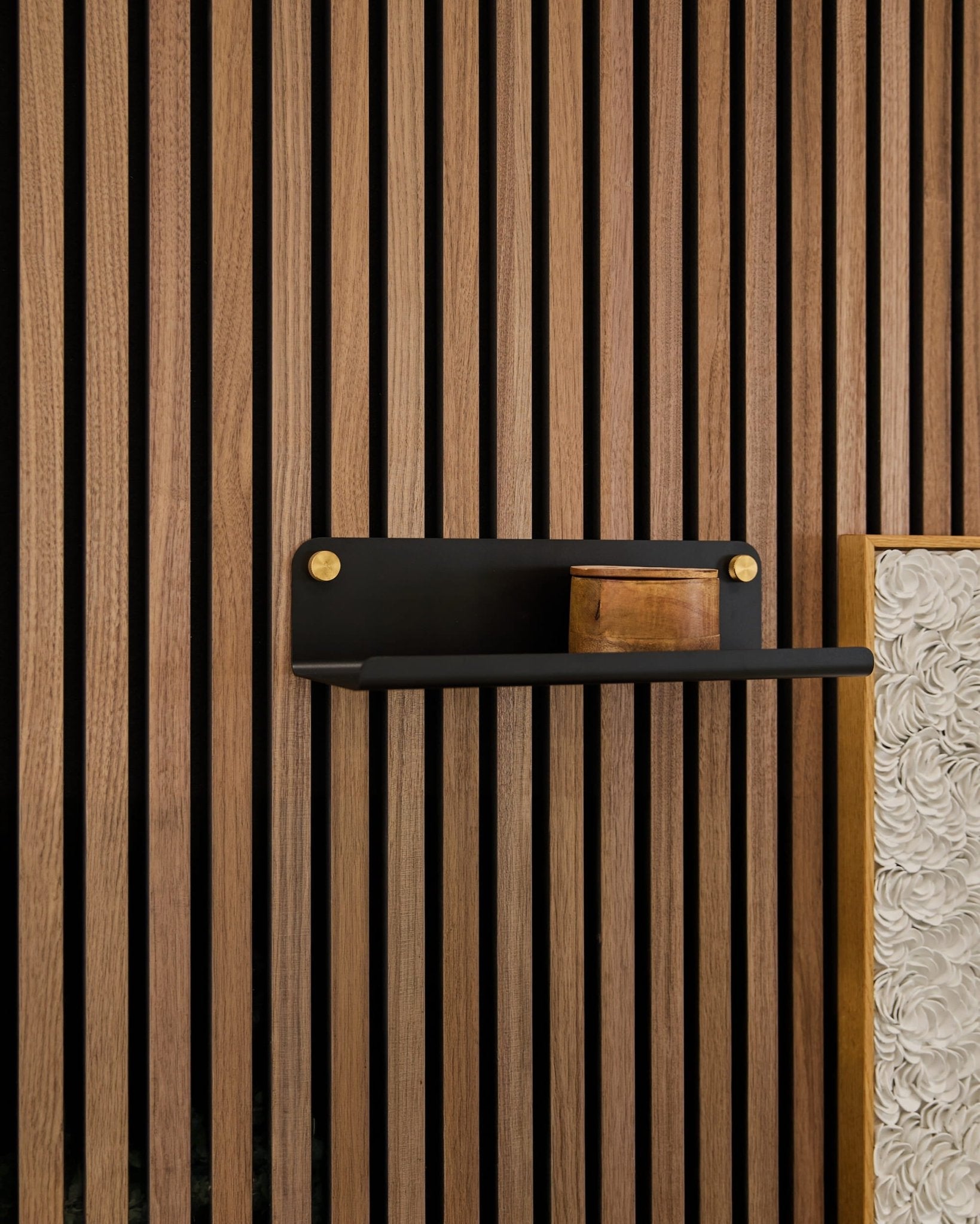 A small wooden box on a WoodUpp Norr Wide Shelf (Black, 35.9 cm) mounted against vertical Akupanel acoustic wood slats, with a textured white panel visible.