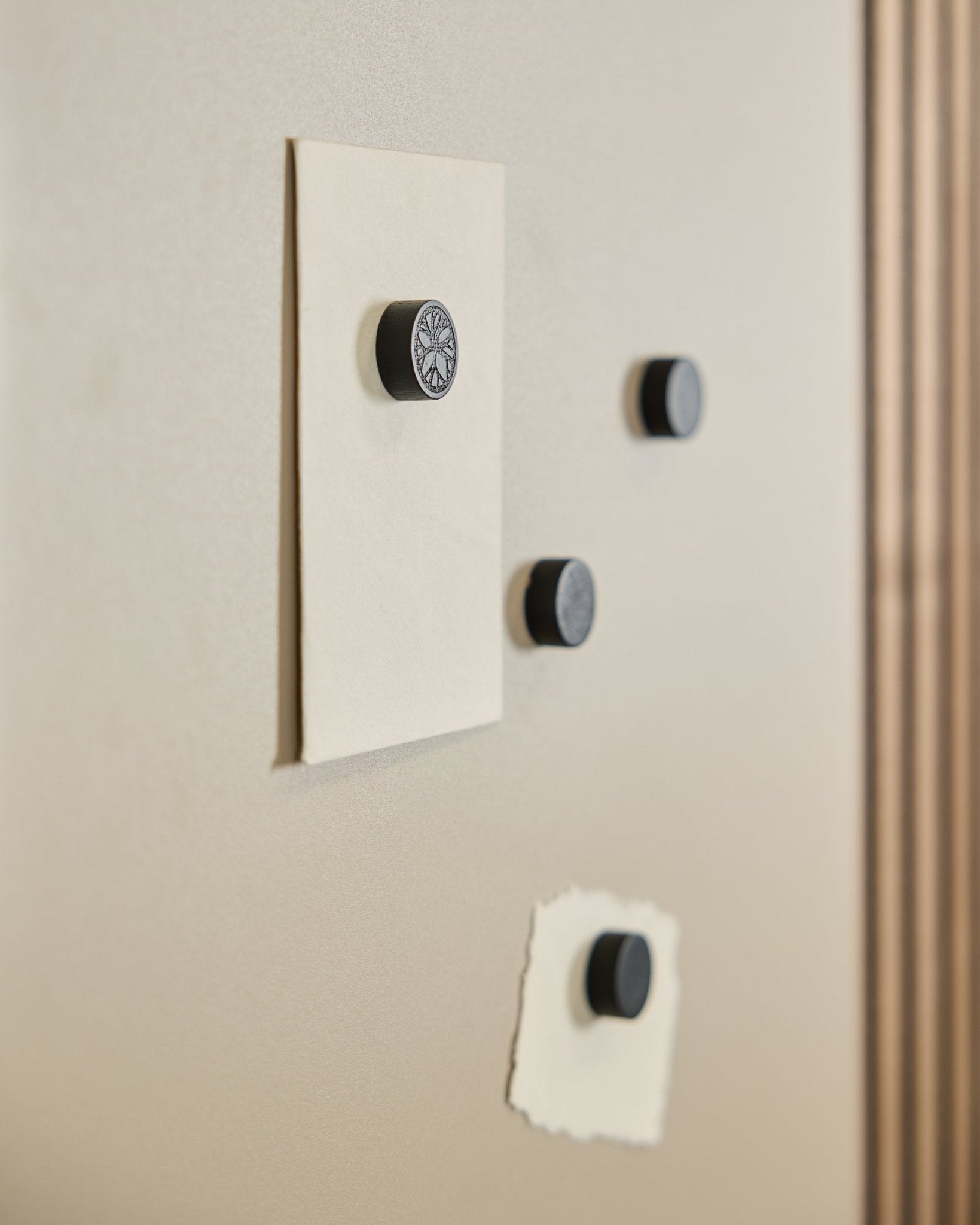 Four WoodUpp Norr Magnet set in Black Oak (4 pcs) secure two papers on a Norr Magnetic Board, with part of an acoustic panel visible on the right.