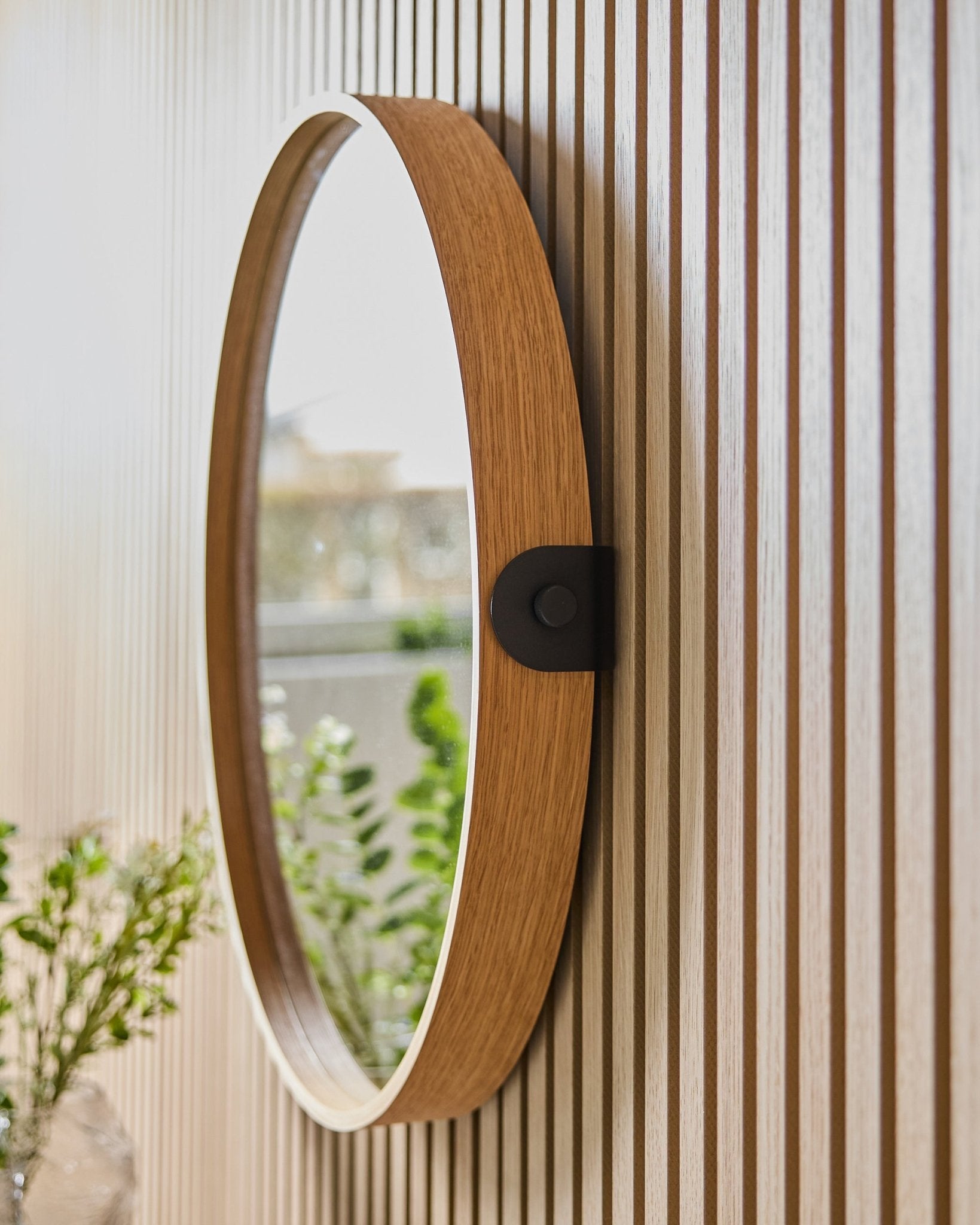 Linn | Mirror / Natural Oak by WoodUpp mounted on a striped acoustic panel wall, reflecting greenery and natural light from a nearby window.