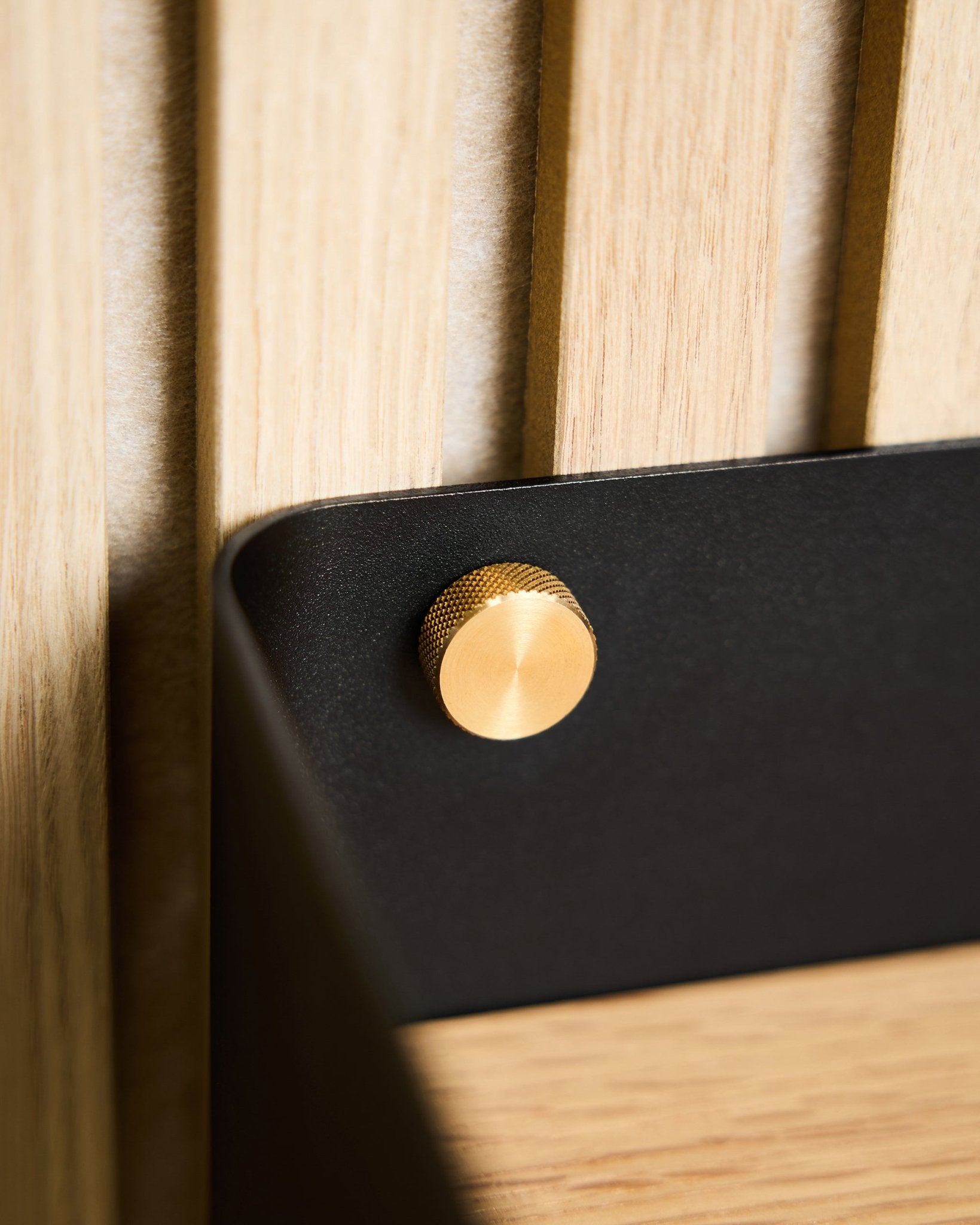 Close-up of two brass WoodUpp Finger screws (M5x10mm, 20x8.8), attached to a black bracket mounted on a light Nordic wood acoustic panel surface.
