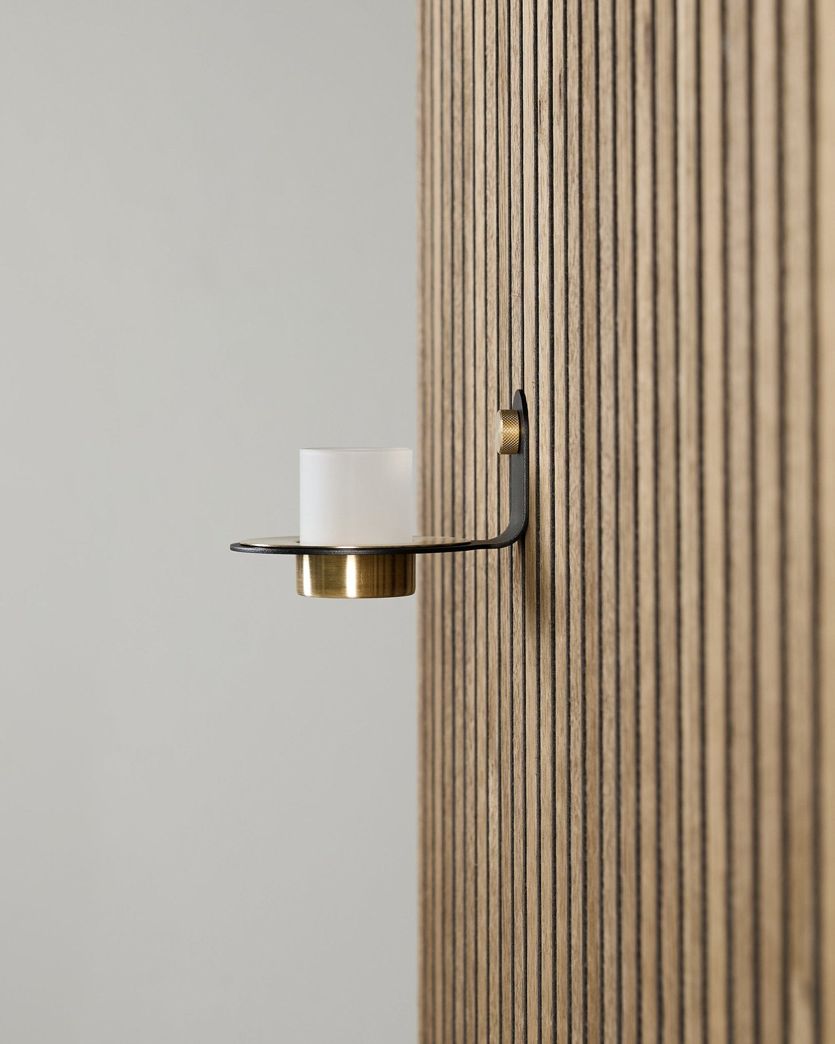 Norr Candle Holder in black and brass from WoodUpp mounted on a vertical Akupanel acoustic panel, featuring frosted glass and brass detailing.