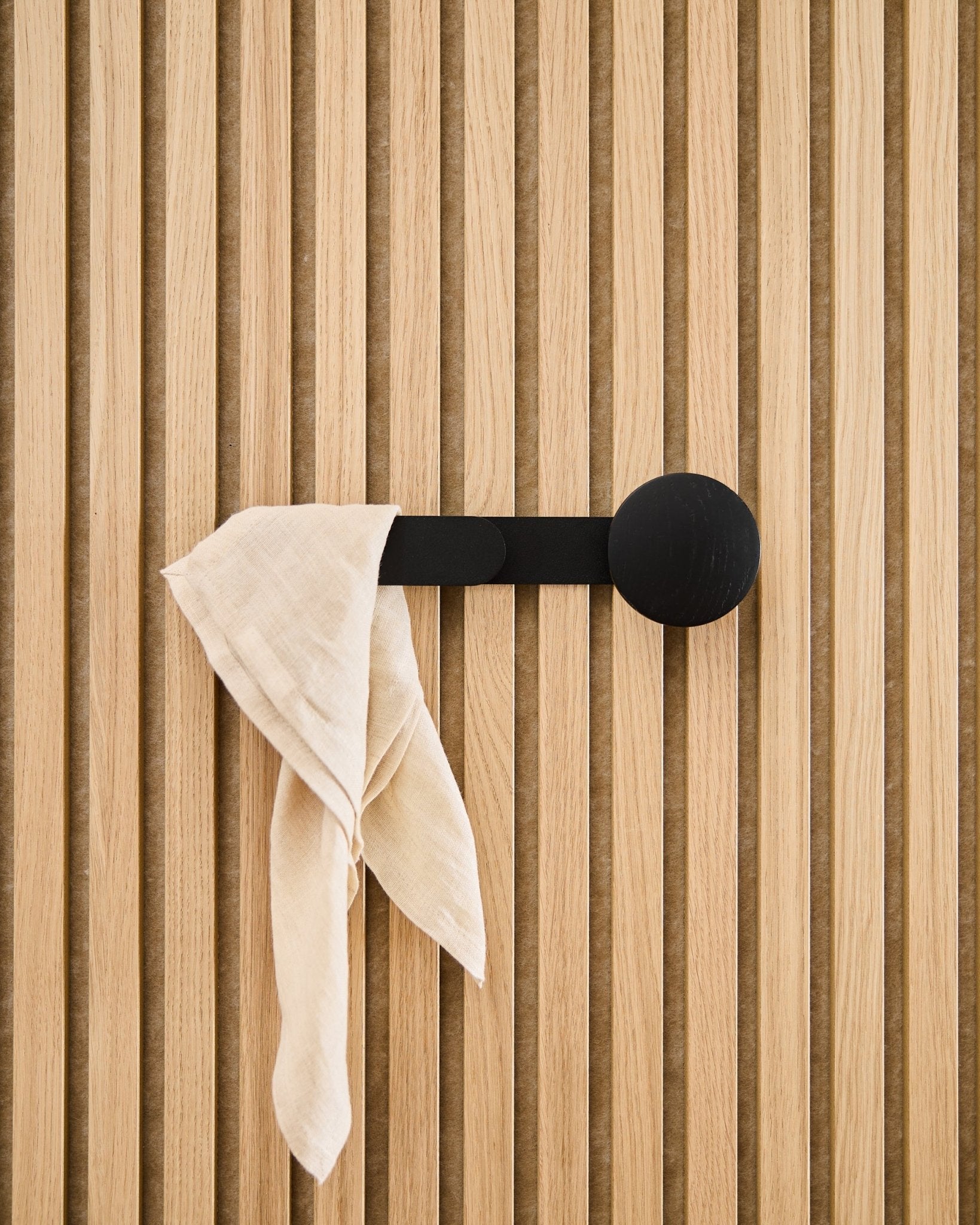 A beige cloth drapes over the WoodUpp Linn Horizontal Hanger in Black Oak, attached to a vertical acoustic slatwall panel.