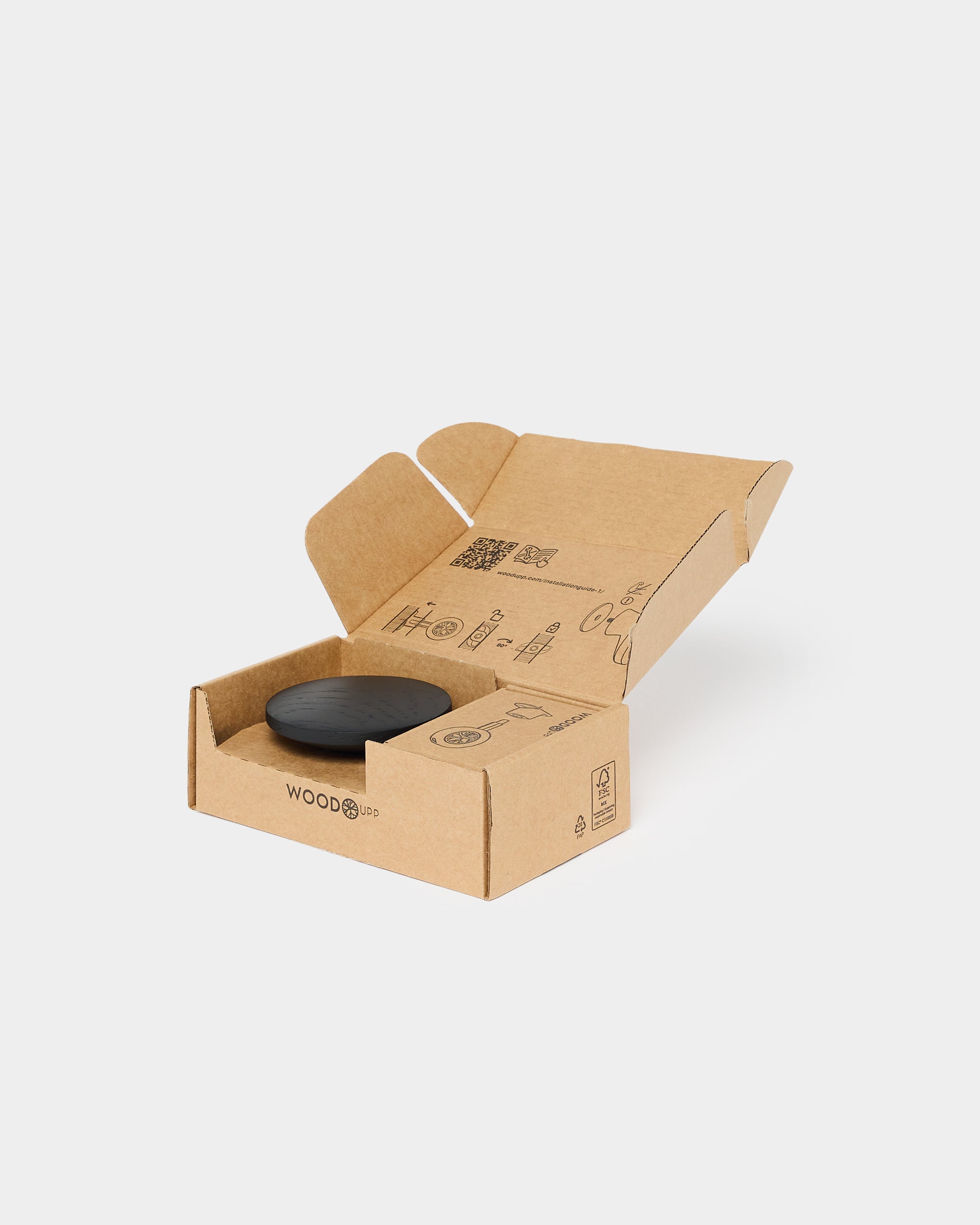 A brown cardboard box with printed icons sits open, revealing a round black accessory for acoustic panels inside, set against a plain white background.