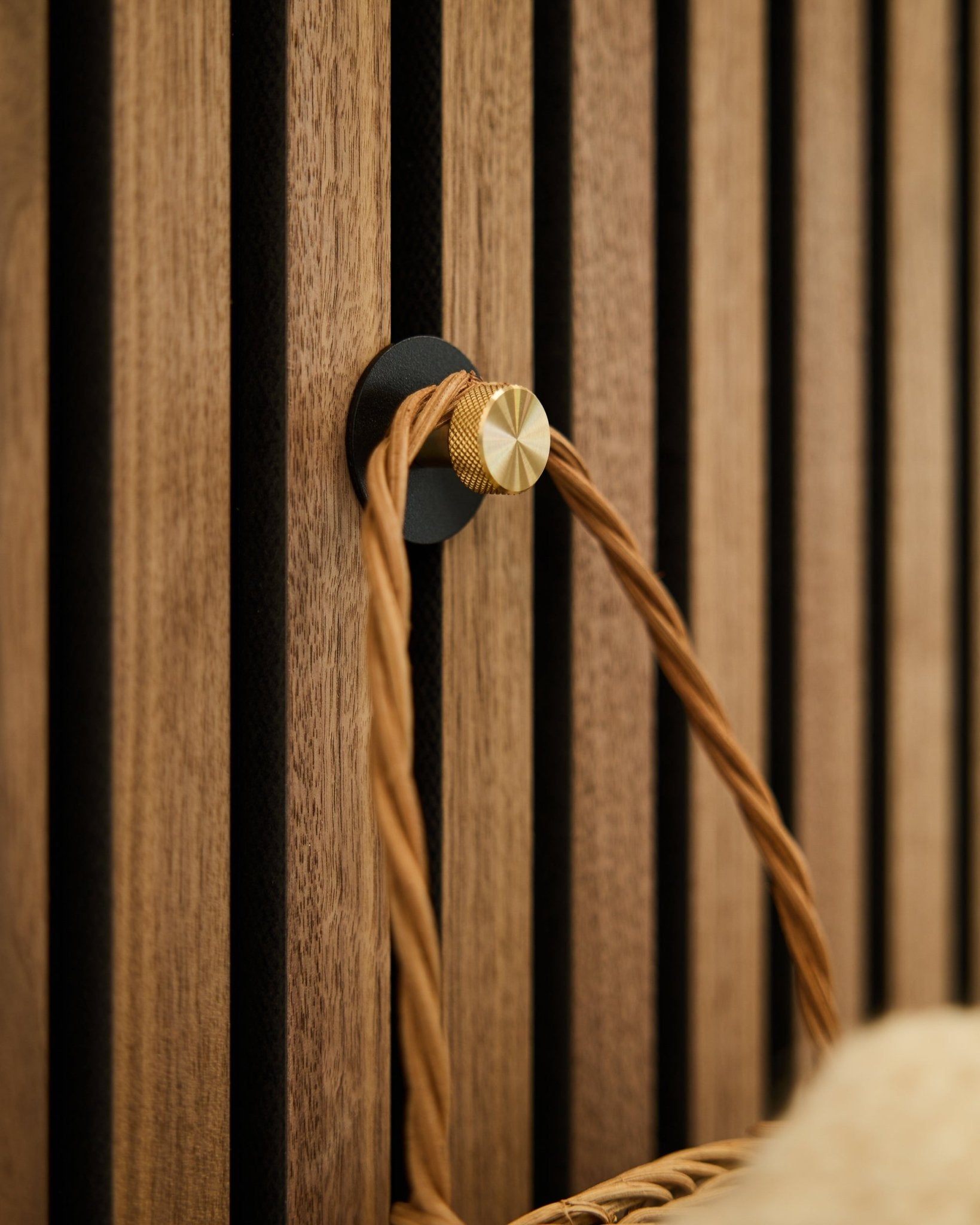 WoodUpp Norr coat hook in black and brass, mounted on a wooden Akupanel acoustic panel, holds a tan braided handle.