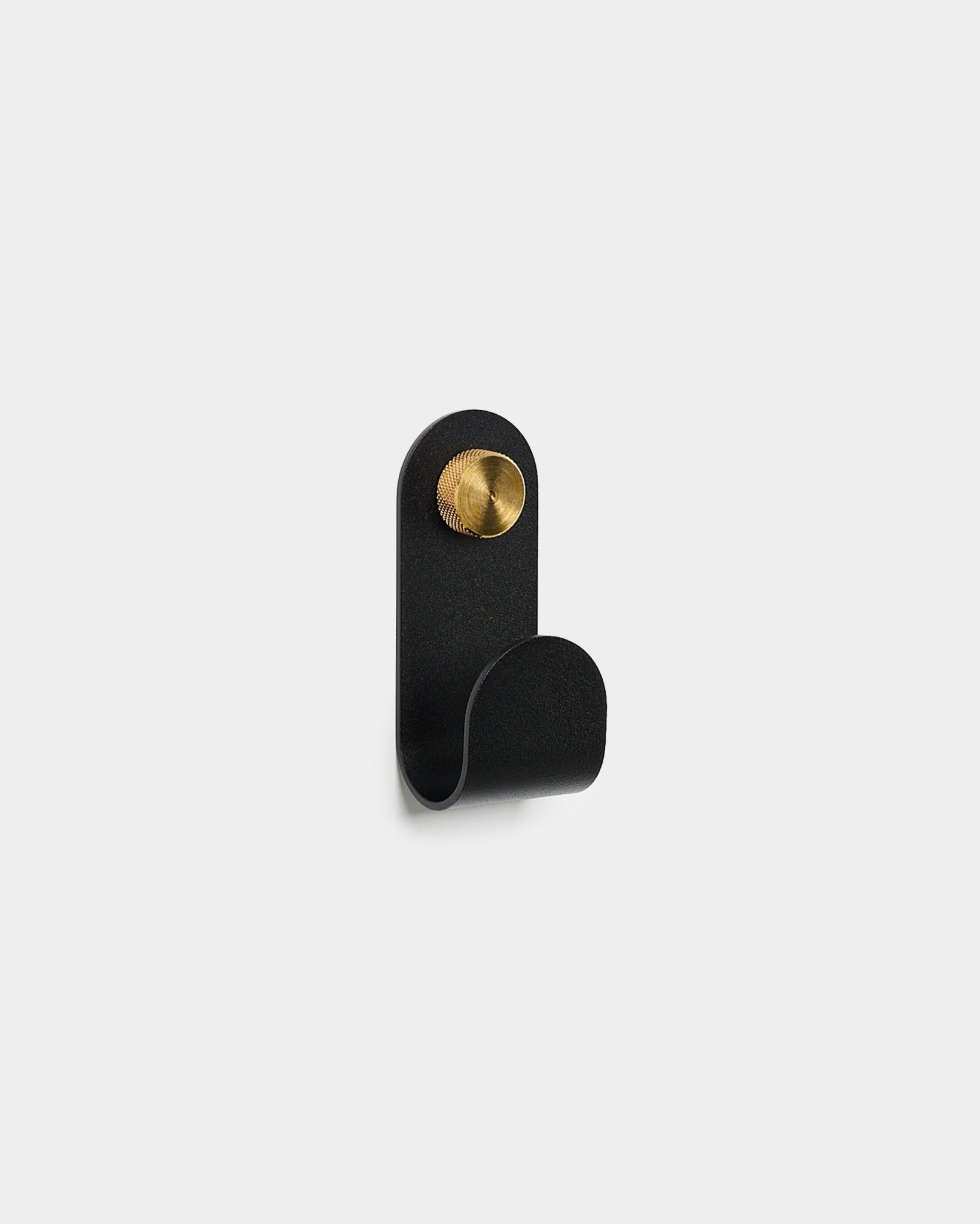 The Norr Single Hanger in black by WoodUpp, with a curved design and round brass accent, displayed against a plain white background.