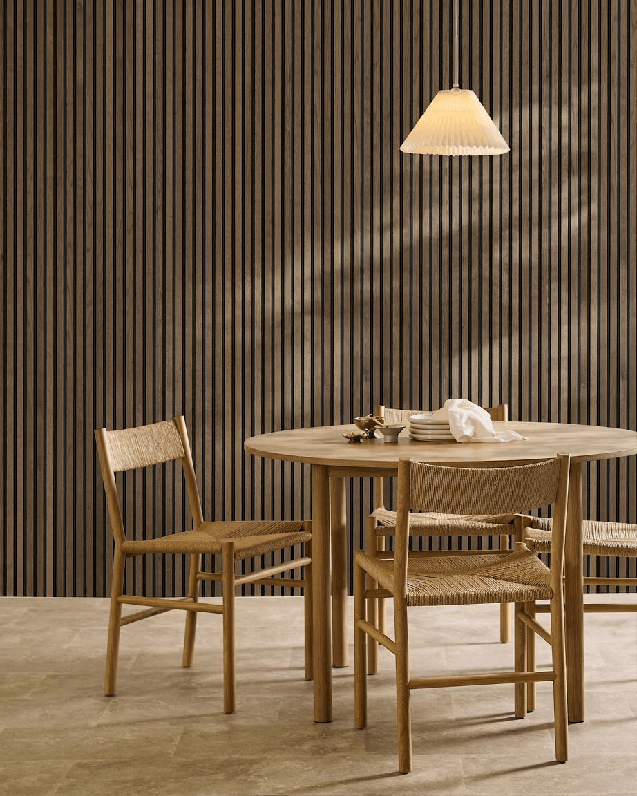 Minimalist dining area with round table, woven chairs, and pendant lamp, featuring a WoodUpp Akupanel Rustic Grey Oak acoustic slatwall panel.