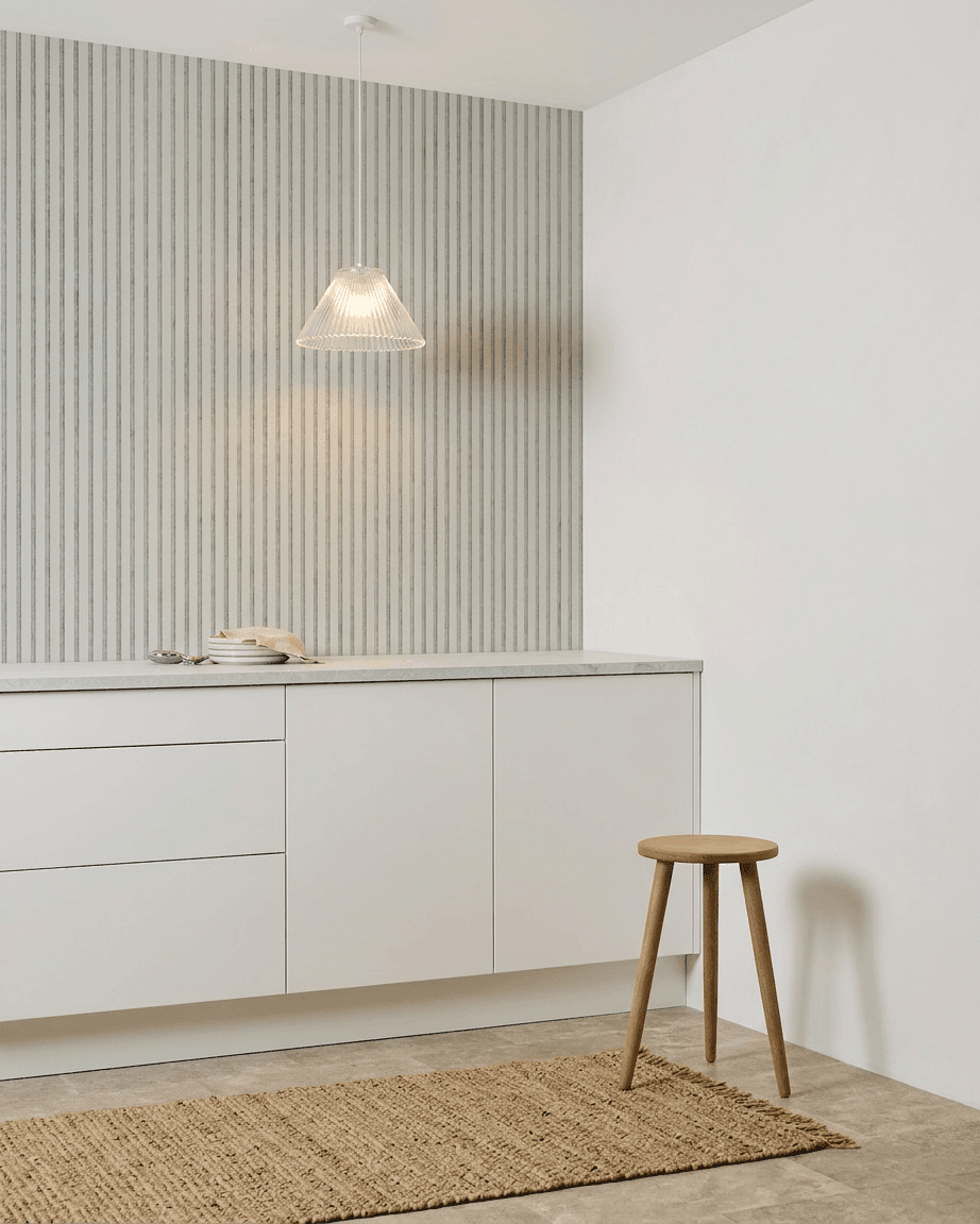 Minimalist kitchen with white cabinets, wooden stool, woven rug, and a WoodUpp Akupanel Snow acoustic panel installed for sound absorption.