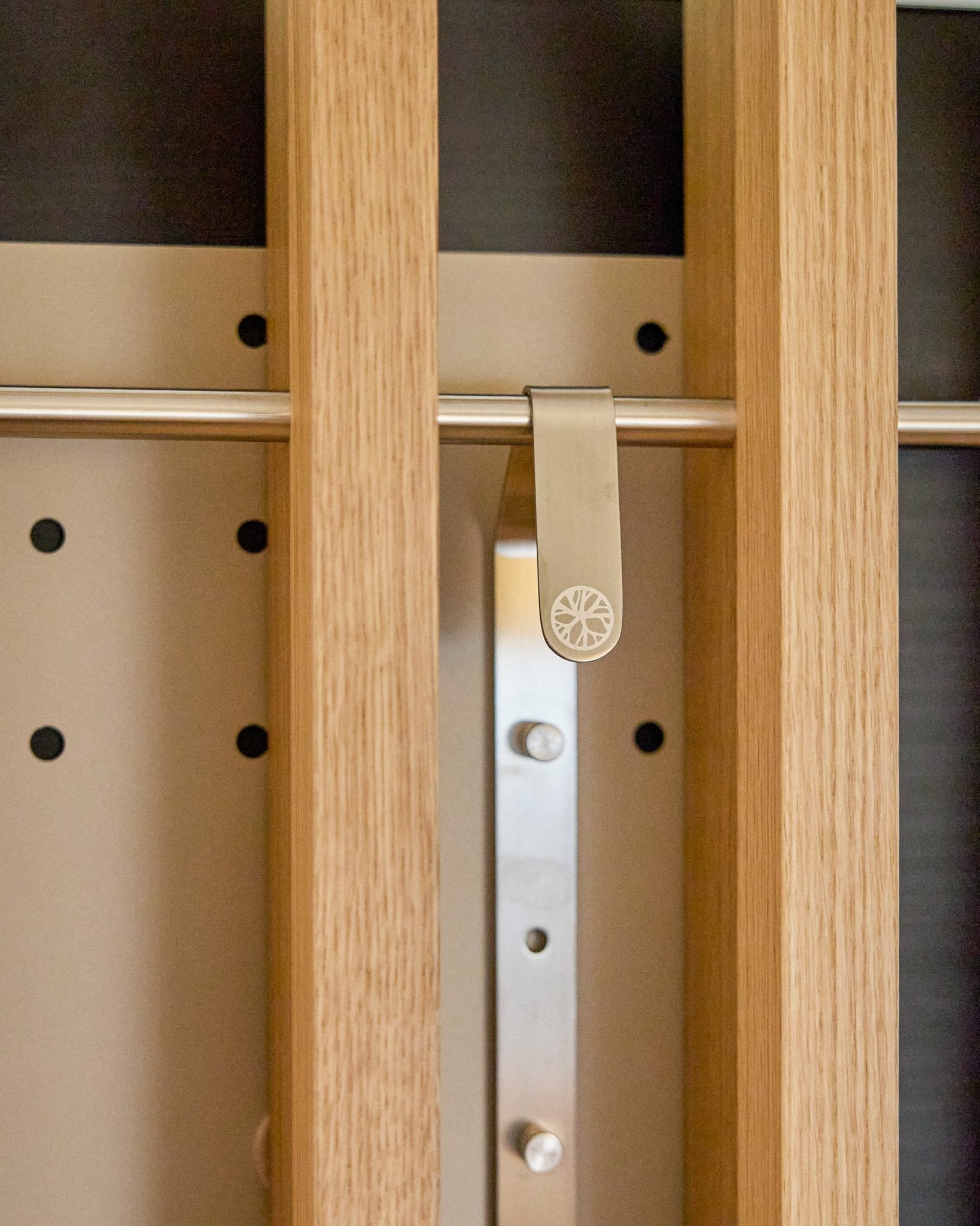 A metal sunburst clip attached to a wooden slat on the WoodUpp Nell | TV-Mount BM1, Beige, 64x44 cm acoustic panel cabinet with height adjustment.