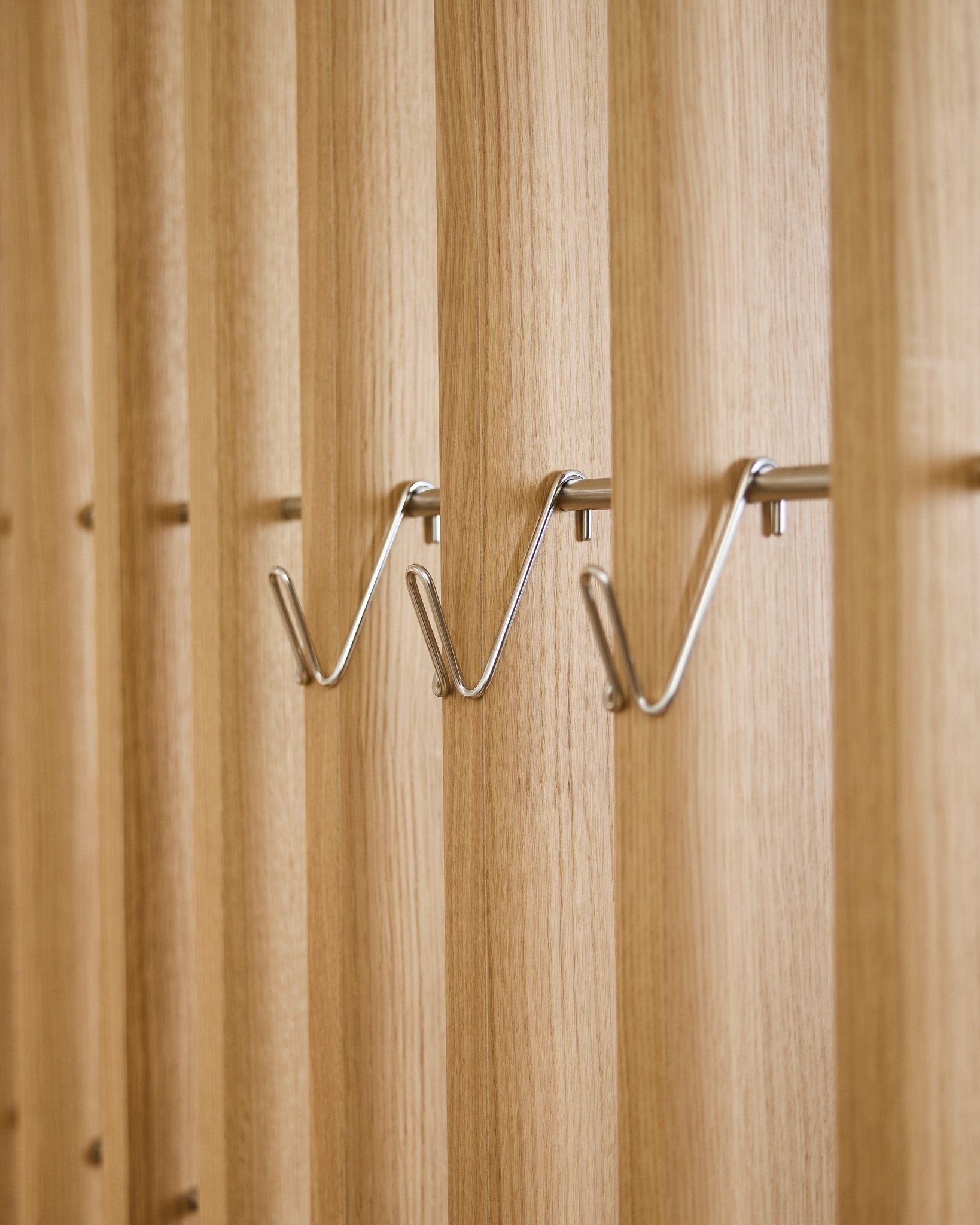 Three short stainless steel WoodUpp Alva Wire Hook / BM1 accessories are evenly mounted in a row on a vertical acoustic wood slat panel.