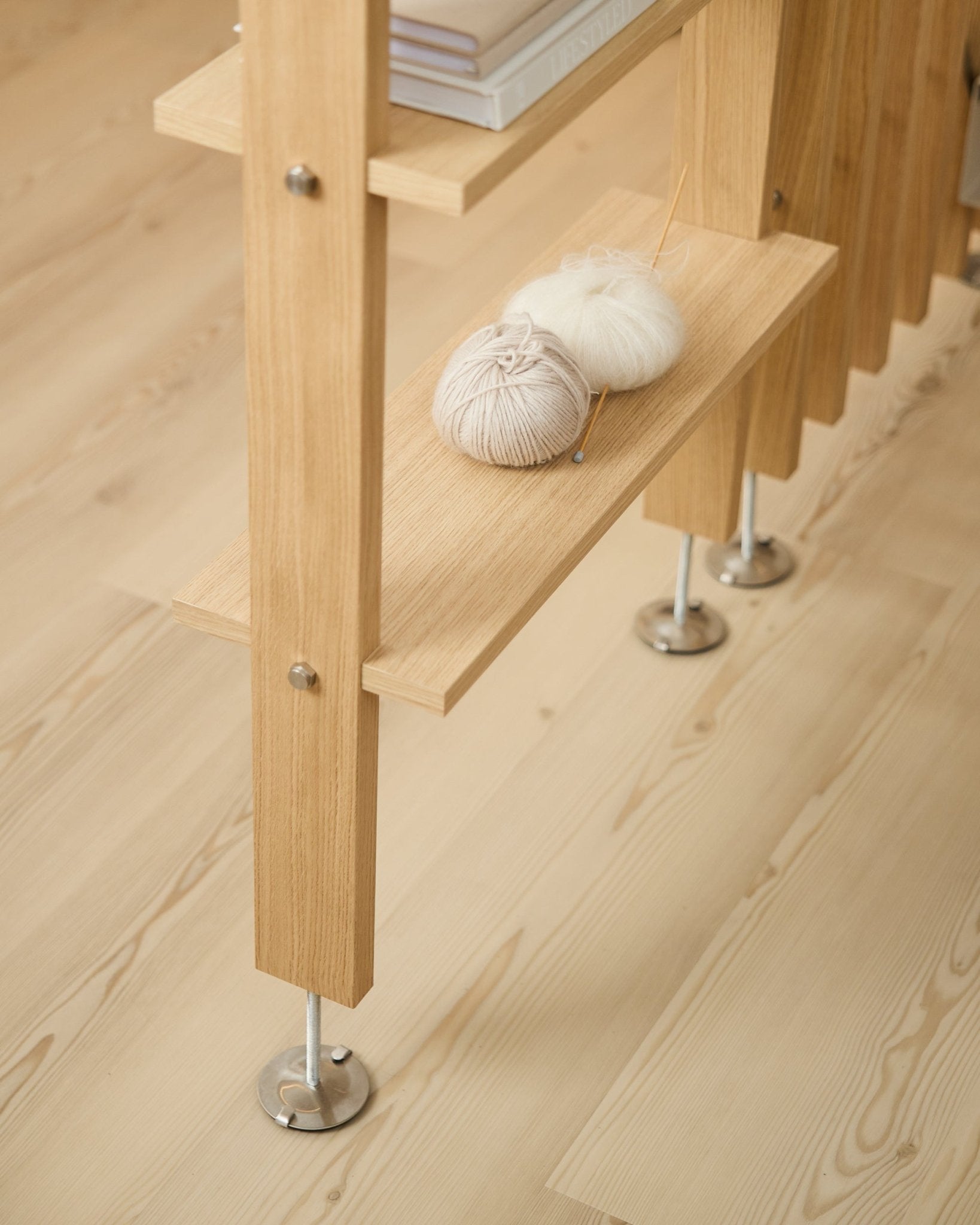 The Lova | Wood Shelf / BM2 by WoodUpp in oak veneer (65.8x20 cm), with yarn and needles on the lower shelf, on a light wood floor with metal feet.