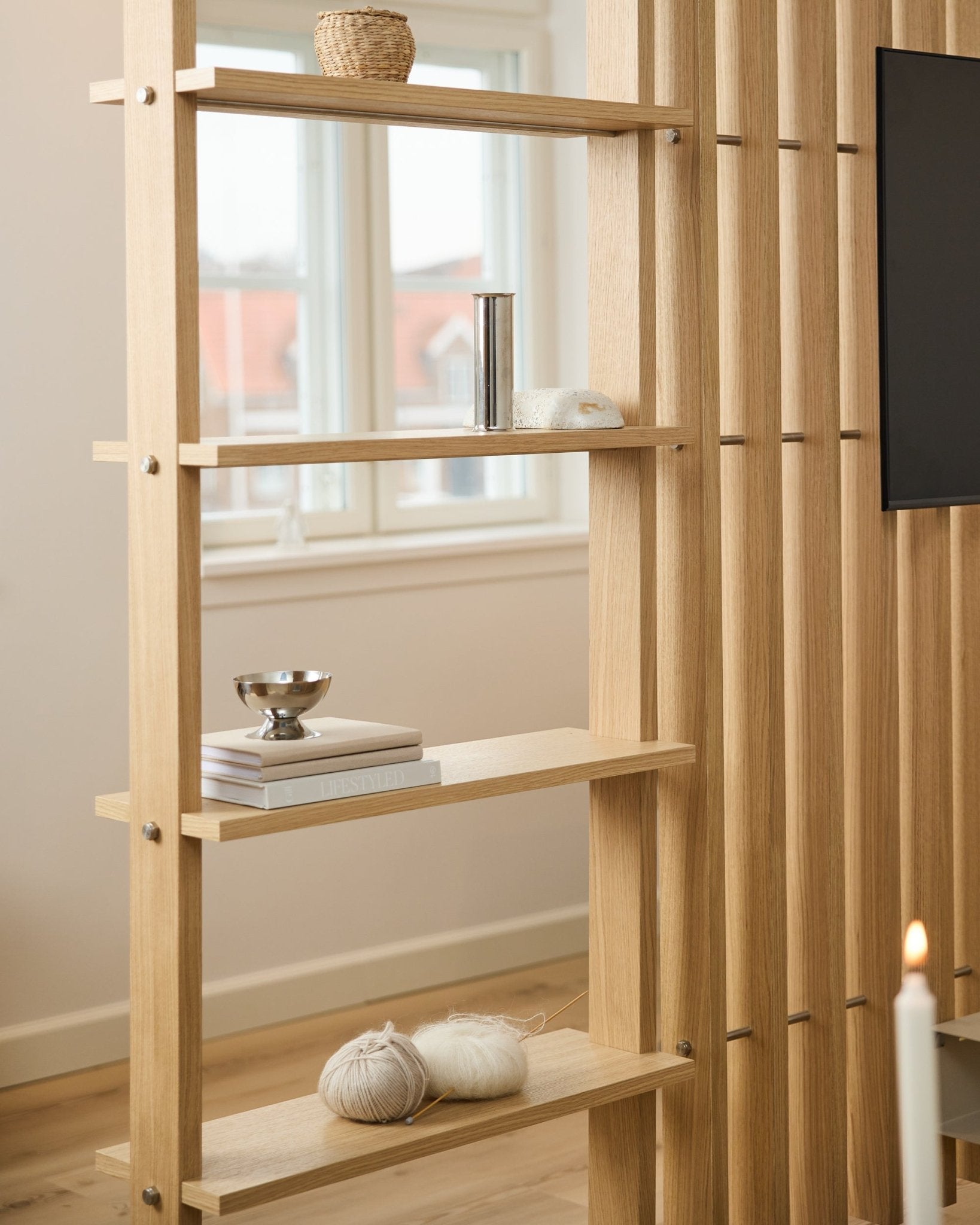 Light oak wood room divider by WoodUpp, with vertical slats and shelves holding books and knitting yarn.